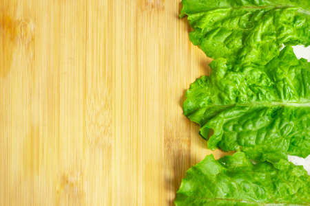 Loose leaf lettuce close up. Top view green lettuce leaves on wooden table. Natural green frame. Restaurant menu concept with copy space.の写真素材