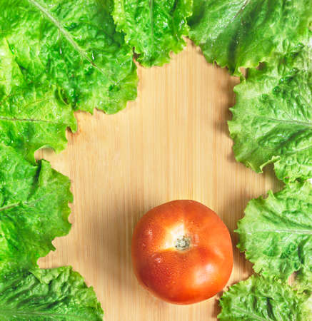 Top view green lettuce leaves with fresh tomato on wooden table. Natural green vegan frame. Restaurant menu concept with copy space. Loose leaf lettuce.の写真素材