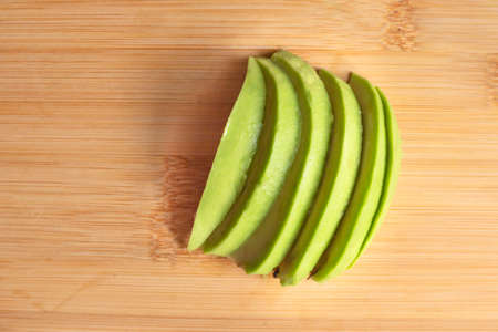 Avocado slices on wooden desk in the kitchen close up top view. Organic tasty alligator pear. Vegan diet ingredient. raw fruit cooking. healthy food conceptの写真素材