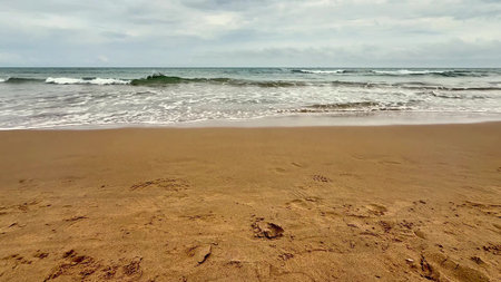 A tranquil coastal scene with gentle waves lapping golden sands under a cloudy sky filled with soft...