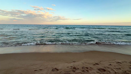 A breathtaking view of a beautiful sunset casting vibrant colors over calm ocean waves lapping...