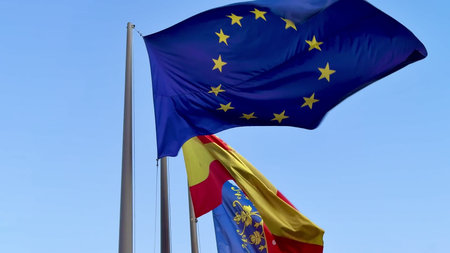 The flags of the European Union and Spain are proudly waving together against a clear blue sky...