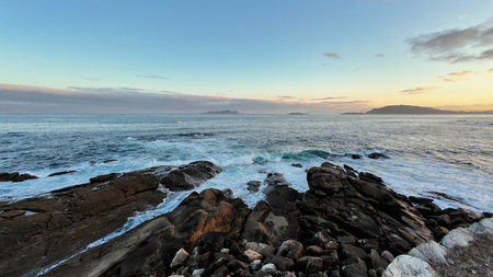 A serene coastal scene with gentle waves crashing against rocks at sunset, showcasing natures beauty