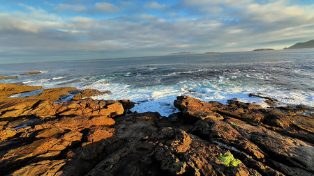 A breathtaking coastal landscape vividly showcasing dramatic rocky shores and ocean waves beneath a...