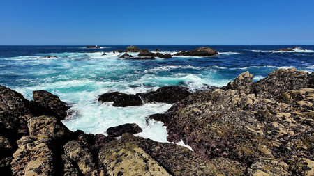 Behold the stunning and breathtaking view of the wavecrashing rocks on a beautiful sunny ocean day
