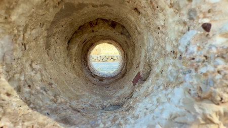 There is a captivating and breathtaking view framed by a circular rock tunnel, showcasing a stunning...
