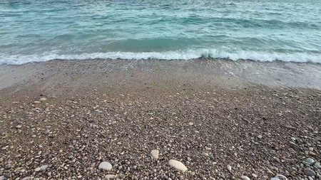 A beautifully calm beach scene that showcases the soft waves gently lapping against a pebblestrewn...
