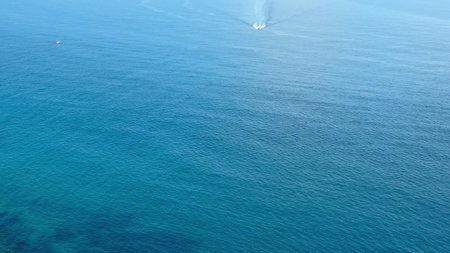 This stunning aerial photo captures serene ocean waves and a boat near a beautiful coastal landscape