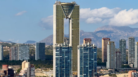 A breathtaking view of a magnificent skyscraper towering among urban buildings under a clear blue...
