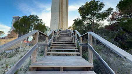 A beautifully crafted wooden staircase gracefully ascends towards a tall and impressive tower,...