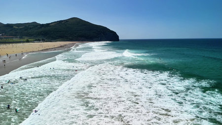 A stunning beach view with vibrant waves crashing gently, and clear blue skies overhead, perfect for...
