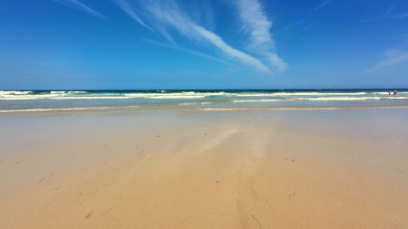 A peaceful and tranquil beach scene featuring soft golden sand and crystal clear blue water beneath...
