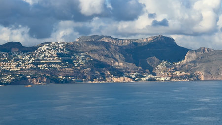 A stunningly beautiful coastal landscape that showcases majestic mountains, fluffy clouds, and...