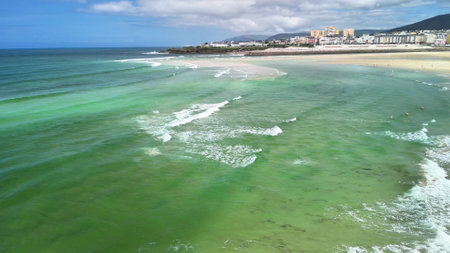 The breathtakingly stunning view of vibrant green ocean waves rolling gently towards the sandy shore on a lovely dayの写真素材