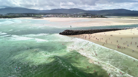 A stunning aerial view captures waves crashing on a vibrant beach where happy people enjoy a sunny...