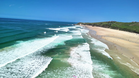 This stunning beach features gentle waves, a radiant sunny sky, and a beautiful sandy shore,...