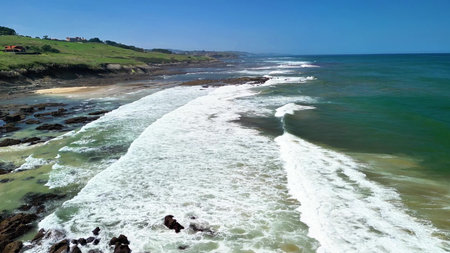 Stunning aerial view of a beautiful coastline, waves crashing against lush green hills under a clear...