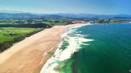 A breathtaking coastal landscape with a stunning sandy beach and rolling waves beneath a clear and bright blue skyの写真素材