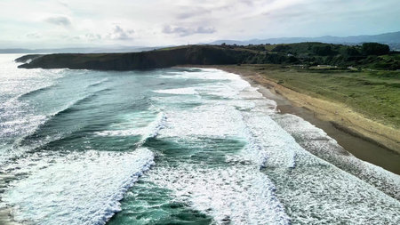 Aerial footage beautifully captures waves crashing against a tranquil and serene beach, showcasing...