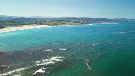 A breathtaking aerial photograph captures the serene blue ocean and the lush, vibrant coastline beneath a clear skyの写真素材