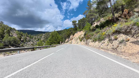 Discover a beautiful and winding mountain road, winding through lush greenery beneath a dynamic, colorful skyの写真素材