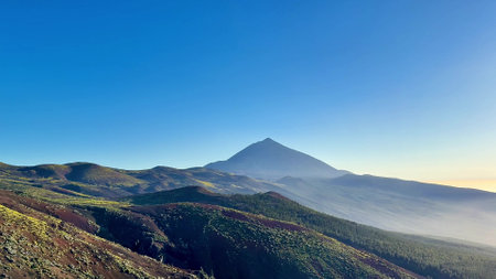 A breathtakingly stunning view of Teide Volcano beautifully framed by lush green hills and clear blue skiesの写真素材