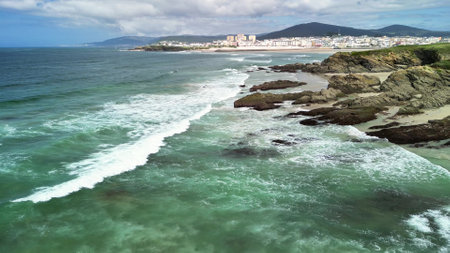 A beautiful coastal scene featuring waves, rocky shores, and a distant city skyline under blue skies.の写真素材