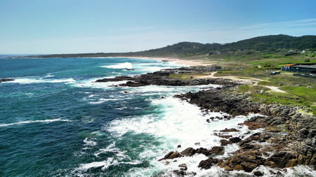 Capture the breathtaking beauty of the coast with waves dramatically crashing upon the rocky shores beneath clear skiesの写真素材