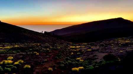 A breathtaking sunset casts vibrant colors over a tranquil mountain landscape rich with lush vegetationの写真素材