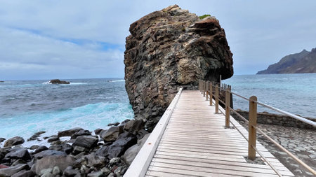 Take a leisurely stroll along a breathtaking coastal walkway that leads to a majestic rock formation by the seaの写真素材