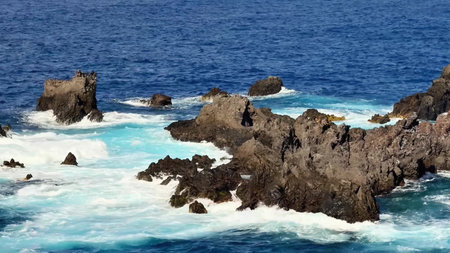 A breathtaking ocean scene featuring dramatic rocky outcrops and powerful crashing waves in vibrant blue watersの写真素材