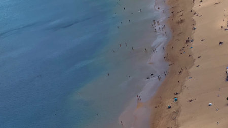 An aerial view shows a busy beach filled with people and vibrant colorful umbrellas along the shoreの写真素材