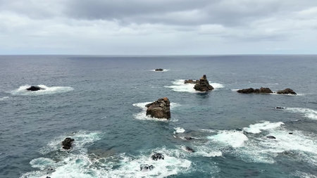 A tranquil and serene ocean view that showcases beautiful rocky islets and calm, gentle waves under a cloudy skyの写真素材