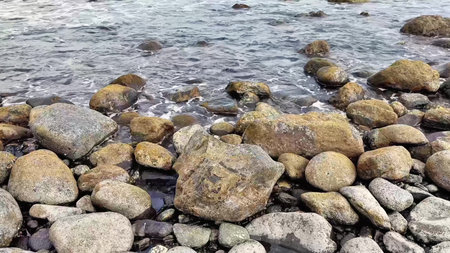 A beautifully tranquil view showcasing rocks lining the idyllic shore with gentle waves lapping...