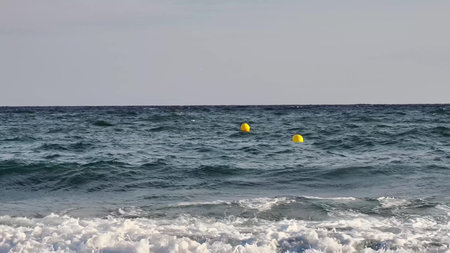 Gentle waves are rolling in on a peaceful ocean scene that features vibrant and colorful yellow buoys floatingの写真素材