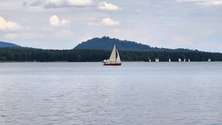 Sailboats gracefully glide across the tranquil waters beneath a cloudy sky, crafting an utterly breathtaking sceneの写真素材