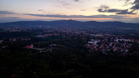 A beautiful aerial view of a vibrant city at twilight, surrounded by lush vegetation and distant mountainsの写真素材