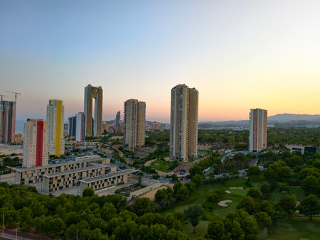 A breathtaking view of modern high-rises against a sunset backdrop, framed by vibrant green landscapes.の写真素材