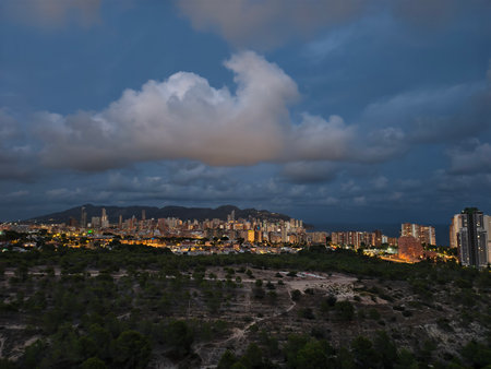 A breathtaking view of a bustling city skyline beautifully illuminated at dusk beneath dramatic, cloudy skiesの写真素材