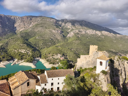 Stunning landscape featuring a picturesque village and castle by a serene reservoir amidst mountains.の写真素材