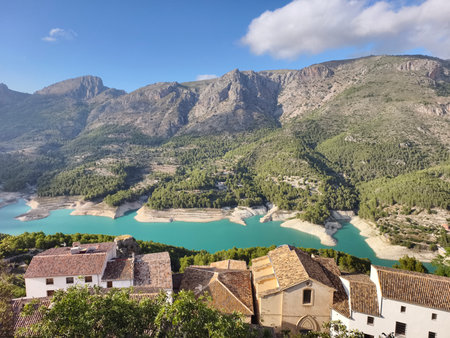 A breathtaking view of majestic mountains, a tranquil lake, and charming rustic houses in a serene idyllic settingの写真素材