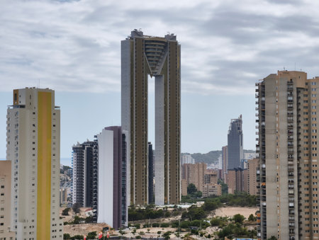 A strikingly beautiful view of a modern contemporary skyscraper set against urban buildings and a cloudy skyの写真素材