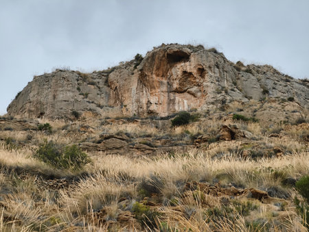A breathtaking and striking rock formation majestically rises, surrounded by grass and dramatic skies overheadの写真素材