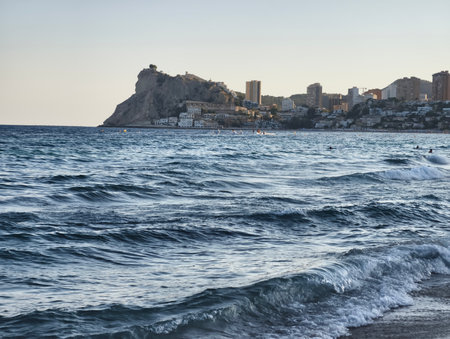 A serene view of majestic waves and a coastal city against a rocky backdrop at dusk, creating tranquilityの写真素材
