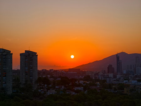 A breathtaking sunset is casting warm and vibrant hues over a sprawling city and distant majestic mountainsの写真素材