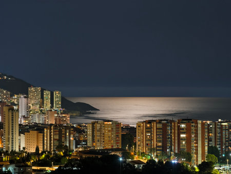 A stunning night view of a vibrant city by the ocean, showcasing illuminated buildings and serene reflection.の写真素材