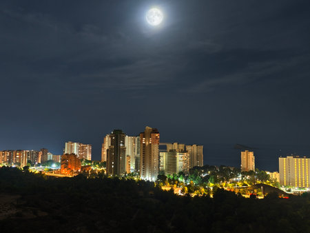 A breathtaking and stunning view of a vibrant city skyline, beautifully illuminated beneath a radiant full moonの写真素材