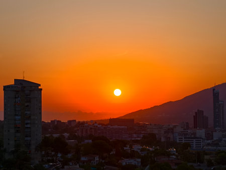 A breathtaking sunset casts vibrant and beautiful colors across both a stunning city skyline and majestic mountainsの写真素材