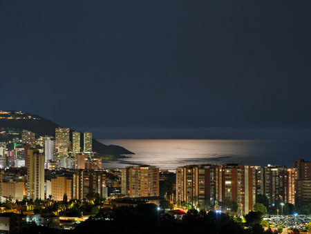 A stunning night view of a coastal city, illuminated with colorful lights reflecting on calm watersの写真素材