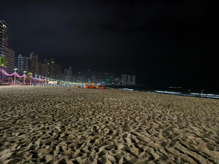 A stunning and breathtaking view of a beautiful beach at night, showcasing vibrant city lights and sandy shorelineの写真素材